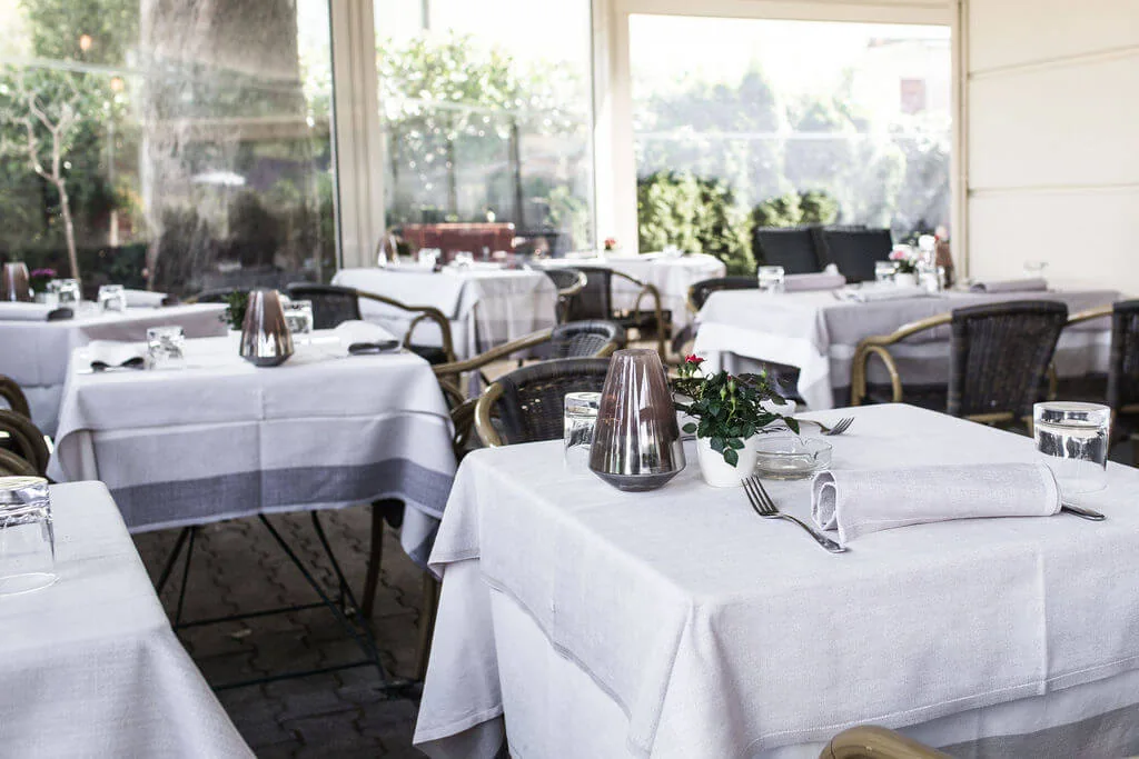 Lichtdurchfluteter Wintergarten der Osteria mit weiß gedeckten Tischen